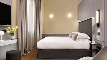 A modern hotel room with a large bed, a flat-screen TV, a bedside table with a lamp, and a small stool.