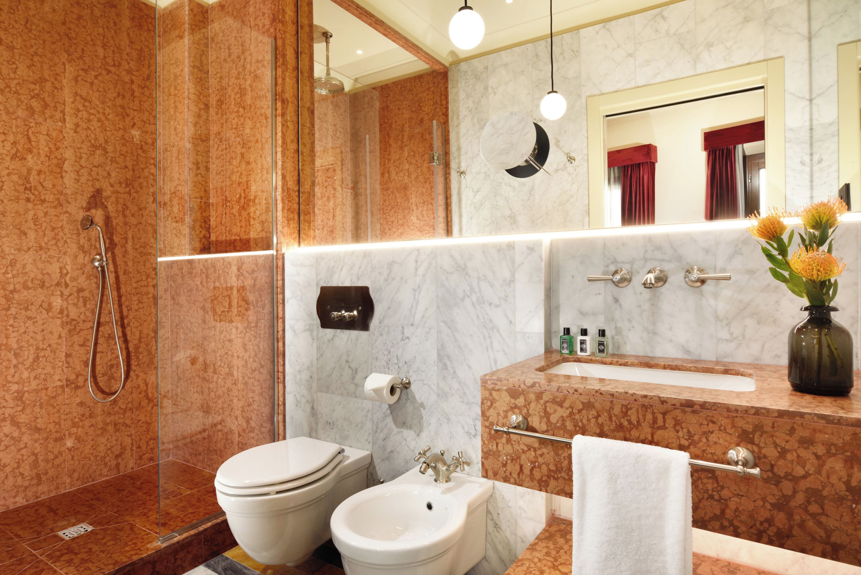 A modern bathroom with a glass-enclosed shower, a bidet, a sink with a vanity, and a mirror with a moon-shaped light fixture.
