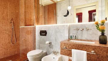 A modern bathroom with a glass-enclosed shower, a bidet, a sink with a vanity, and a mirror with a moon-shaped light fixture.