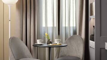 A modern room with two grey upholstered chairs, a small round table with a vase of yellow tulips, two white cups, and a plate of food.