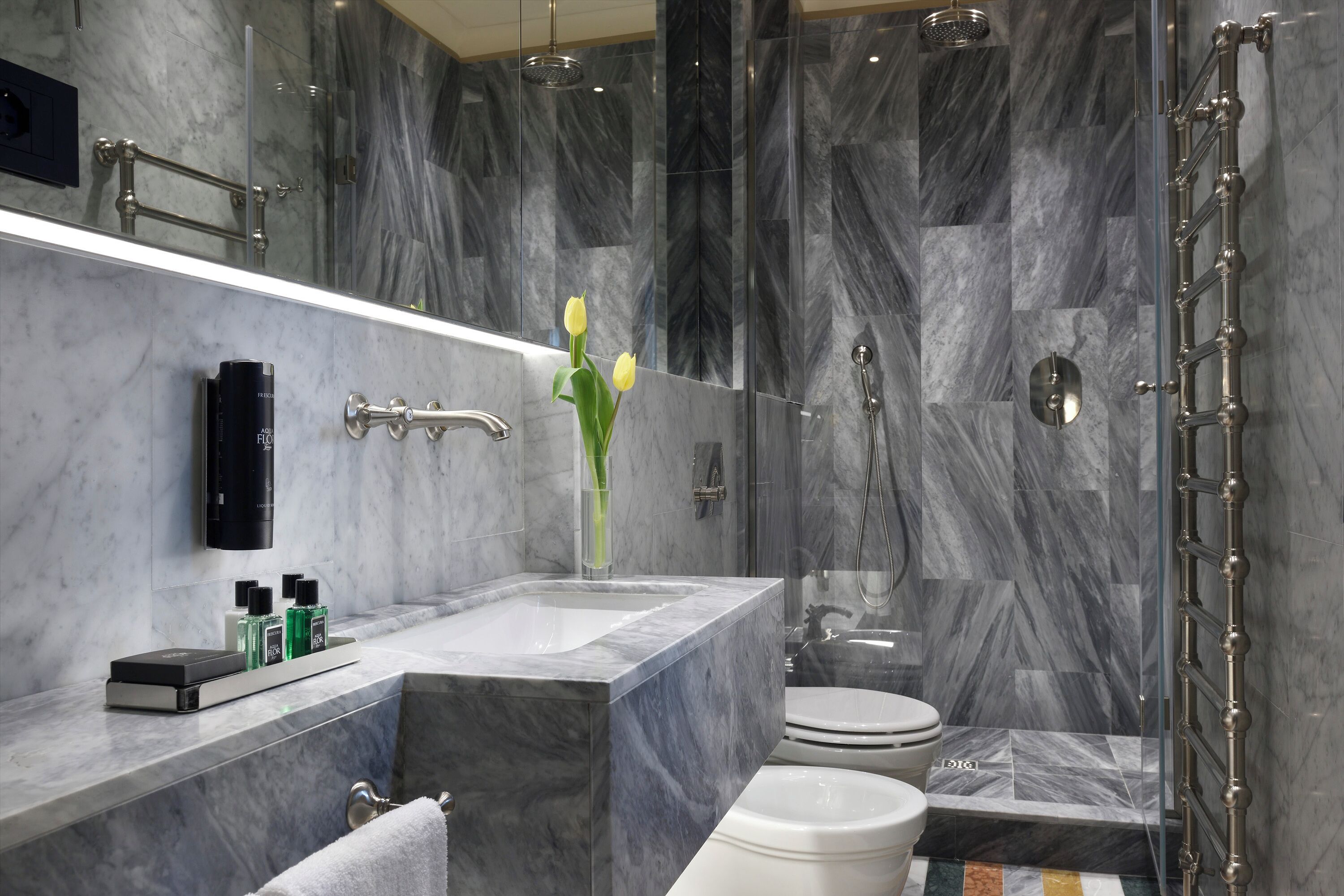 Un bany modern amb un lavabo de marbre, un cubicle de dutxa de vidre i un vàter.