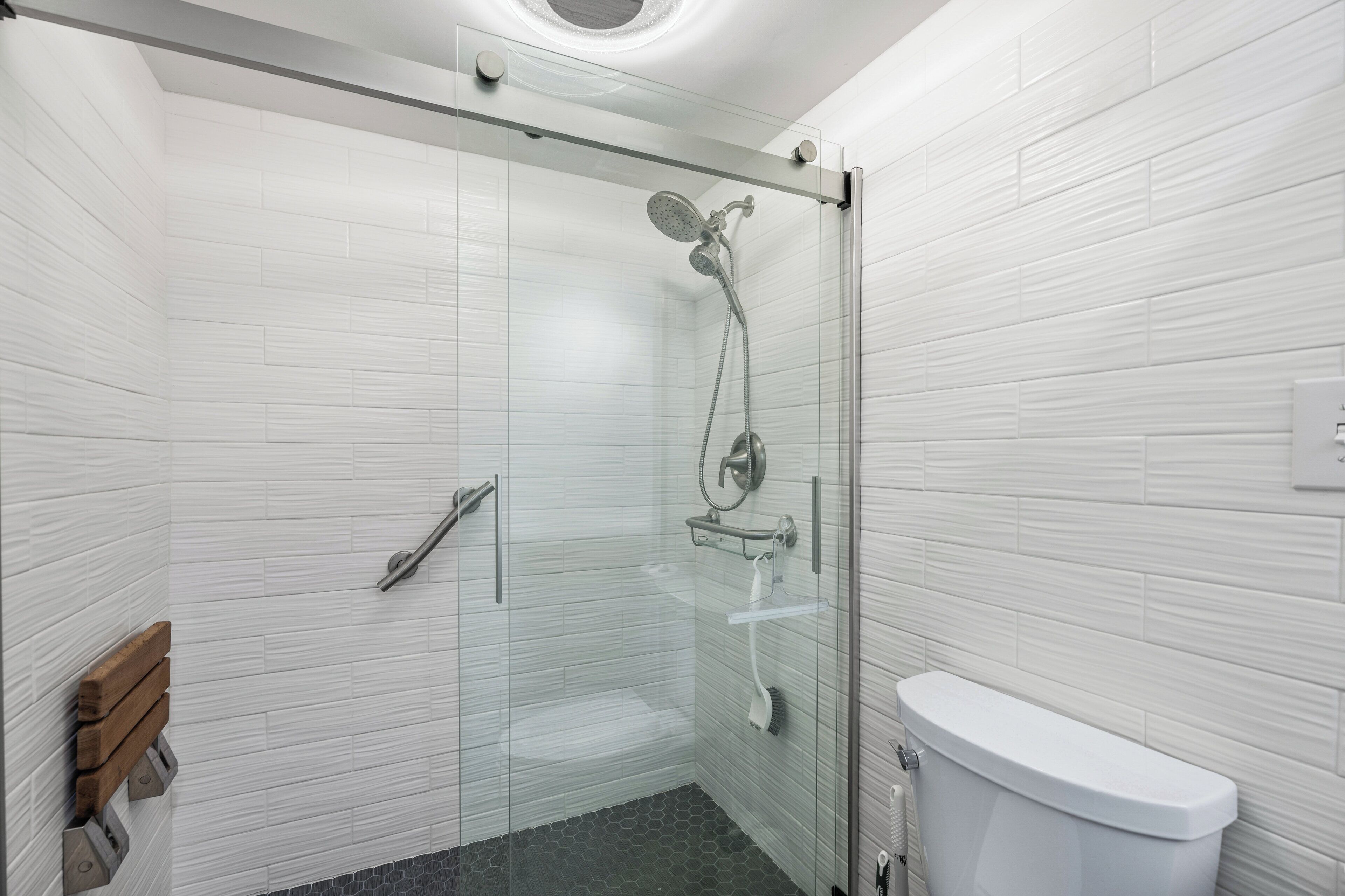 A modern bathroom with a glass-enclosed shower, white tiled walls, and a white toilet.