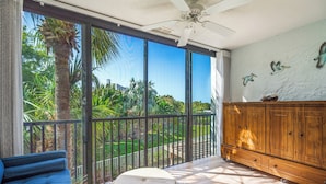 Una habitación con un amplio ventanal corredera que da a un jardín, un ventilador de techo y un mueble de madera con cajones.
