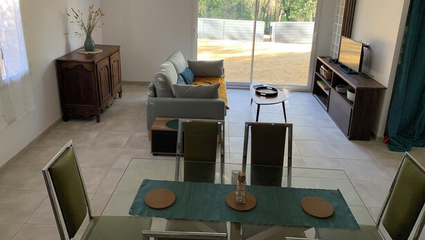 Una sala moderna con sofá, mesa de centro, televisor y comedor con sillas y mesa.