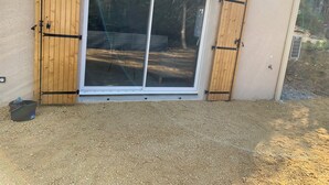 Una puerta corrediza de vidrio con contraventanas de madera, un camino de grava y una valla metálica al fondo.