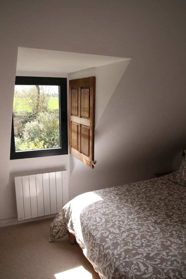 A bedroom with a sloped ceiling, a window, a radiator, and a bed with patterned bedding.