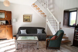A living room with a sofa, armchair, coffee table, wooden staircase, and a bookshelf. - B&B 53 m2 private suite (Pleumeur Gautier)
