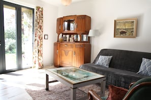 Een woonkamer met een bank, een salontafel met glazen blad, een houten kast en een schilderij aan de muur.