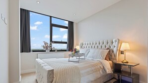 Une chambre moderne avec un grand lit, une table de chevet avec une lampe, une fenêtre avec des rideaux et une vue sur le ciel.