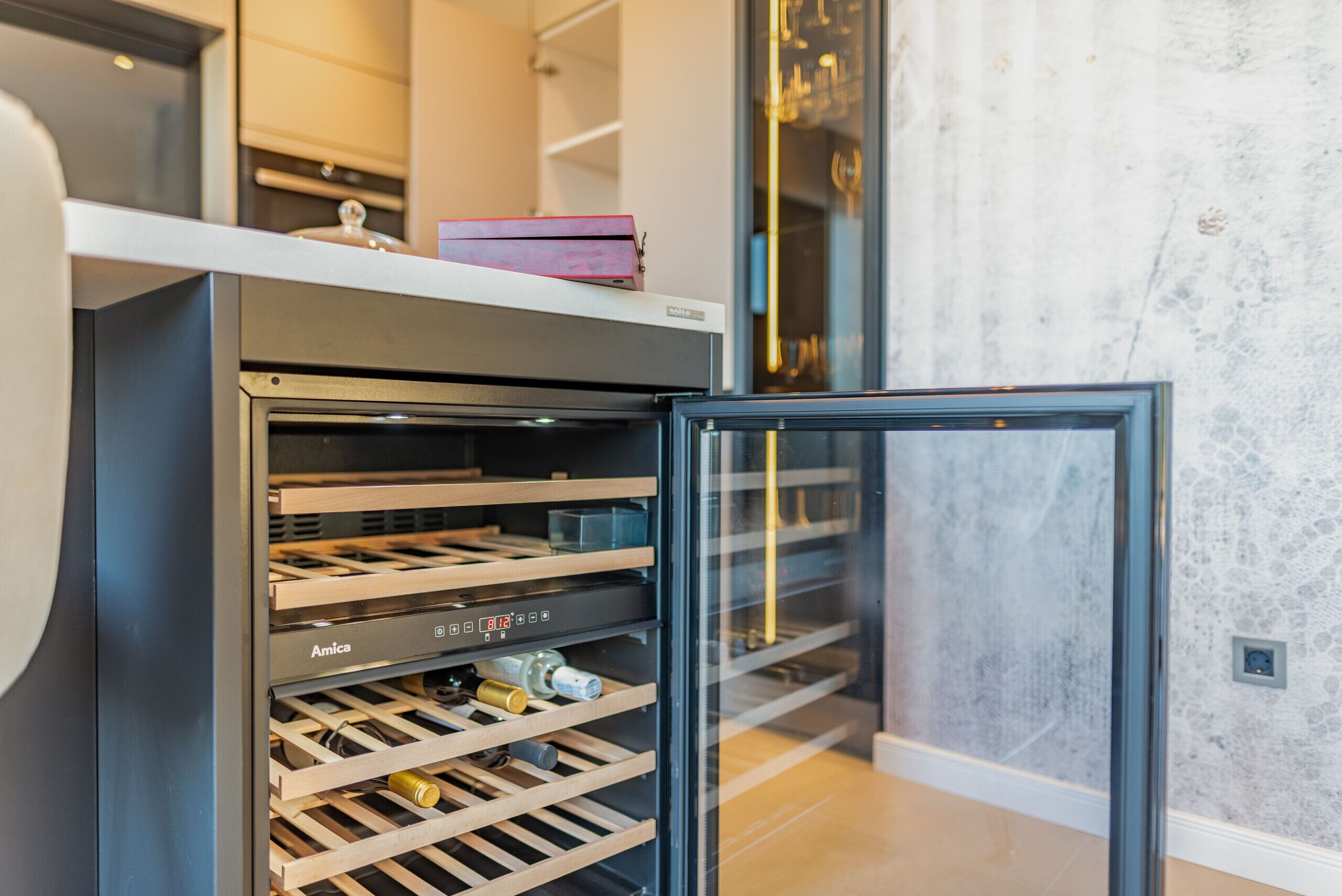 Eine moderne Küche mit integriertem Weinkühlschrank, einem Kühl- und Gefrierschrank mit Glastür und einer Arbeitsplatte mit einem Buch.