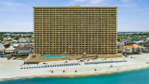 A large hotel with multiple floors, a pool, and a beach area with sun loungers.