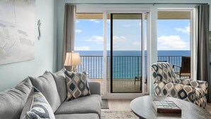A balcony with a view of the ocean, a sofa, a patterned armchair, and a table with a decorative box.