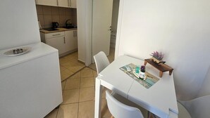 Uma cozinha compacta com armários brancos, uma mesa de jantar com cadeiras e um pequeno aparador de madeira.