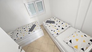 Quarto pequeno e limpo com duas camas de solteiro, uma janela e uma porta.