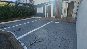 Une cour pavée, agrémentée d’un portail en métal, d’une haie et d’un bâtiment doté d’une porte et de fenêtres blanches.
