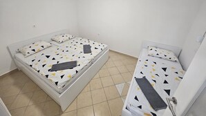 Une petite chambre propre, avec deux lits simples, des murs blancs et un sol carrelé.