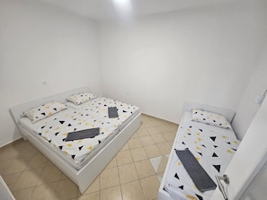 A small, clean room with two single beds, a white door, and a tiled floor.