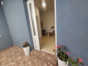 Une pièce avec un sol carrelé, une porte blanche, un bureau avec une chaise et des plantes en pot.