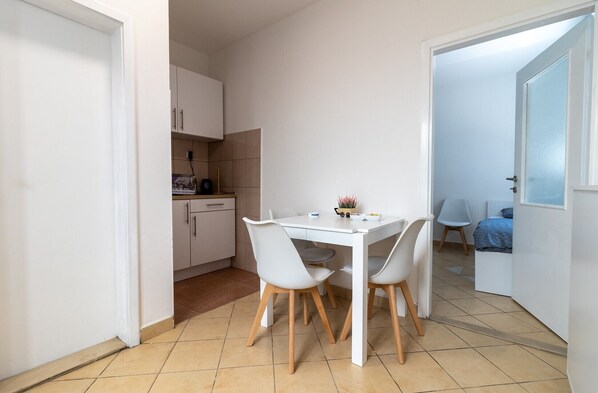 Une cuisine compacte avec des meubles blancs et un coin repas comprenant une table et des chaises blanches.