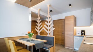 A modern kitchen with wooden cabinetry, a built-in dishwasher, and a dining area with a bench and chairs. - Fantastic vacation in the Dolomites (St. Martin in Thurn)