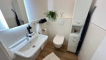 A modern bathroom with a white sink, toilet, and storage cabinet.