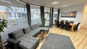 Un espacio de oficina moderno con un sofá seccional gris, una mesa redonda de centro y una zona de comedor con mesa de madera y sillas negras.
