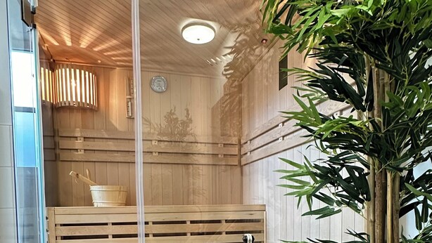 Un sauna moderno con bancos de madera, un separador de vidrio y una mesa con copas de vino y una botella.