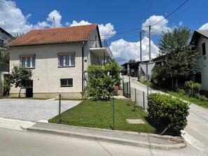 Una casa de dos pisos con techo de tejas, un patio cercado y un pequeño jardín.