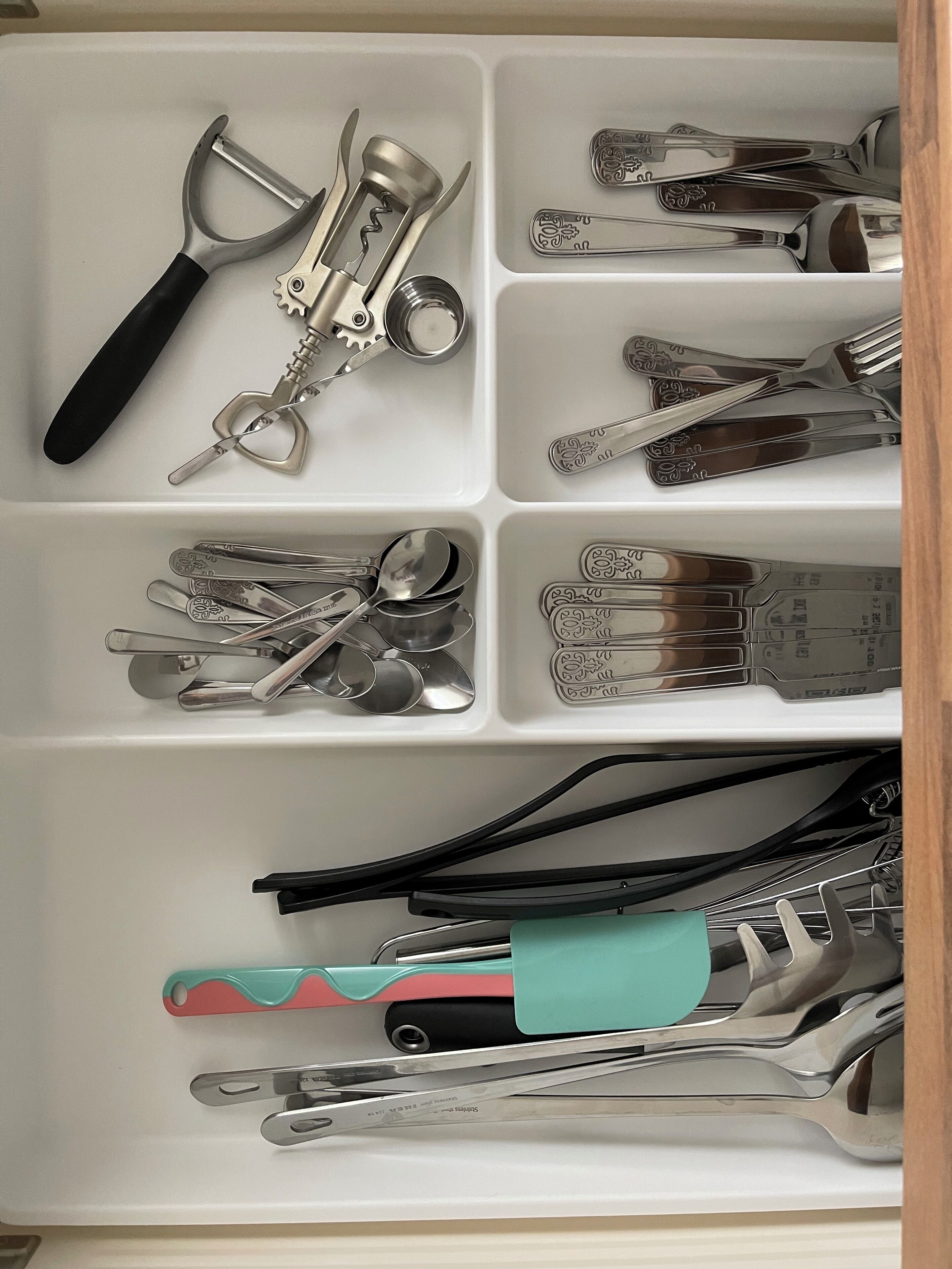 A drawer with compartments containing various kitchen utensils, including a grater, a corkscrew, and a pair of scissors.