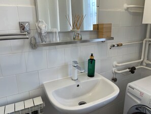 Un baño con un lavabo blanco, un espejo, un inodoro y una lavadora blanca.