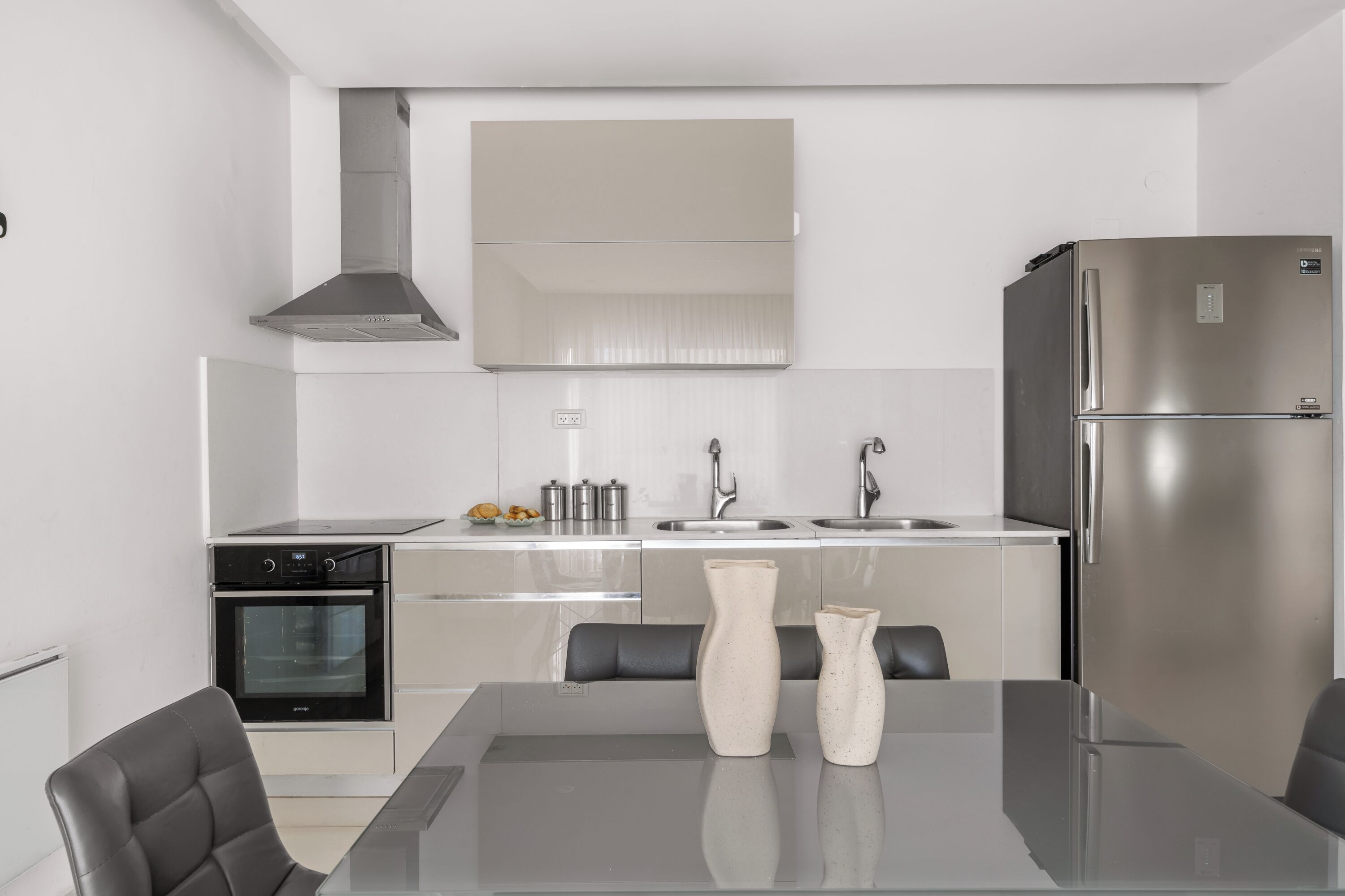 A modern kitchen with stainless steel appliances, a dining table with chairs, and a large mirror above the sink.