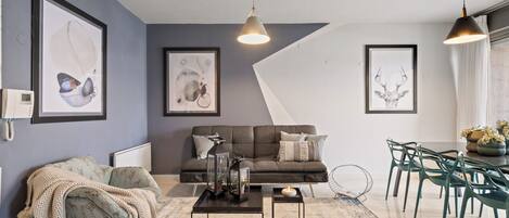 A modern living room with a grey sofa, a coffee table, and a dining area with green chairs.