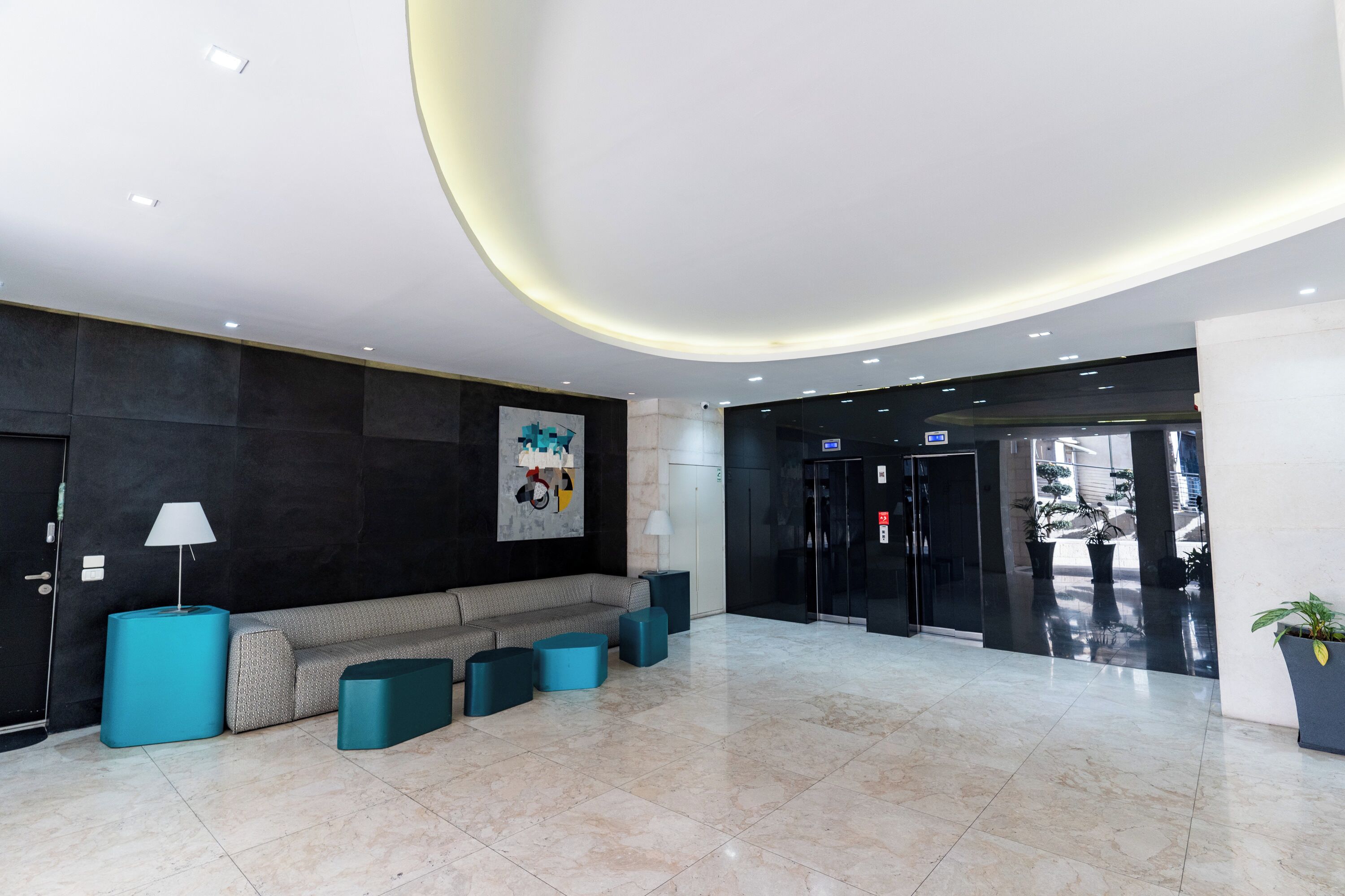 Eine moderne Lobby mit einer Couch, türkisfarbenen Hocker, einer Lampe und einem großen abstrakten Gemälde.