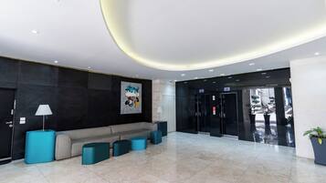Eine moderne Lobby mit einer Couch, türkisfarbenen Hocker, einer Lampe und einem großen abstrakten Gemälde.