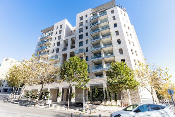 Un edificio residencial de varios pisos con balcones, entrada protegida por un portón y zona de estacionamiento.