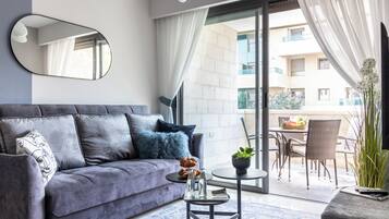 Ein modernes Wohnzimmer mit grauem Sofa, einem runden Couchtisch mit Dekoration und Blick auf einen Außenbalkon mit Korbmöbeln.