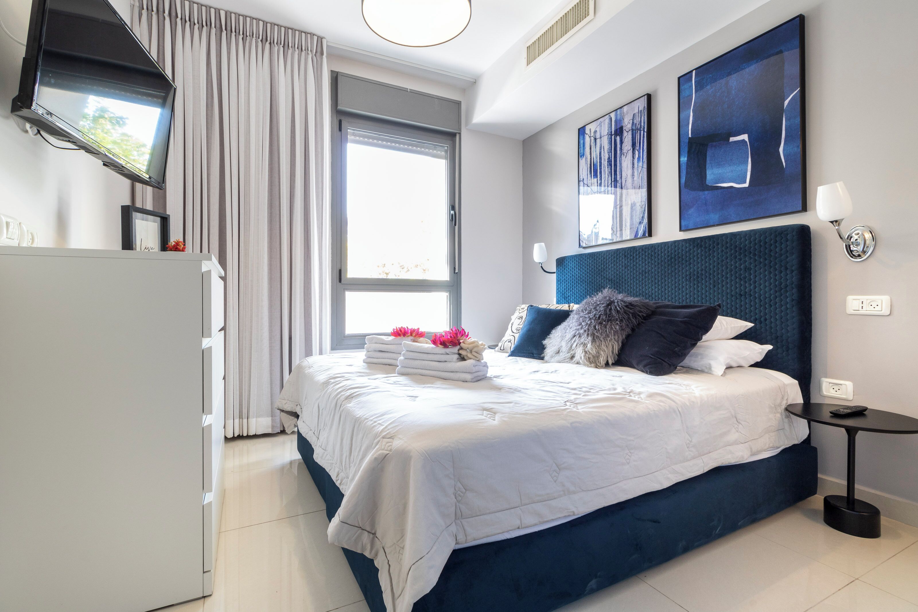 A modern hotel room with a large bed, a flat-screen TV, and artwork on the walls.