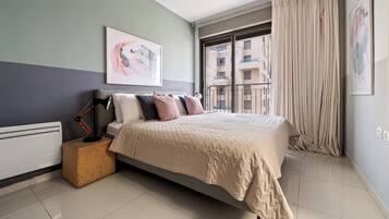 A modern bedroom with a bed, a bedside table, a lamp, and a window with curtains.