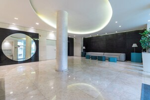 Un vestíbulo amplio con piso de mármol, una columna central, un espejo circular, un sofá y una planta.
