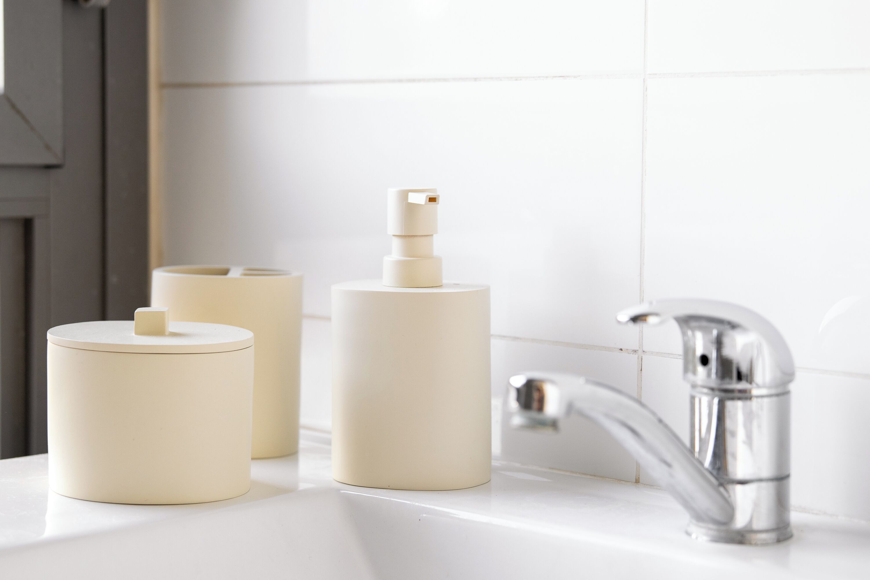 Een badkamer met een witte wastafel, een chromen kraan en drie beige doseerders.