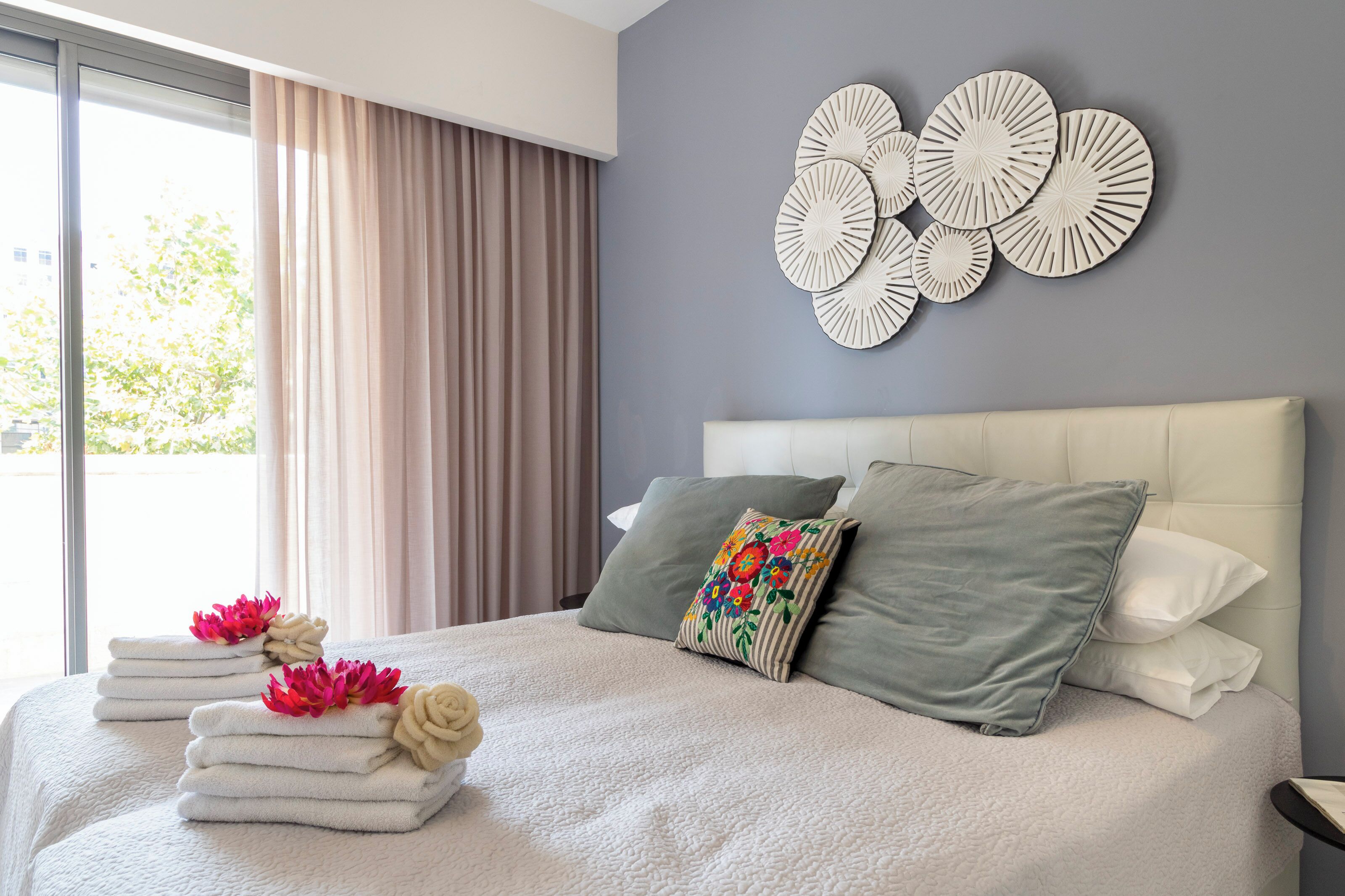 A modern hotel room with a large bed, a view of the outdoors, and a decorative wall piece.