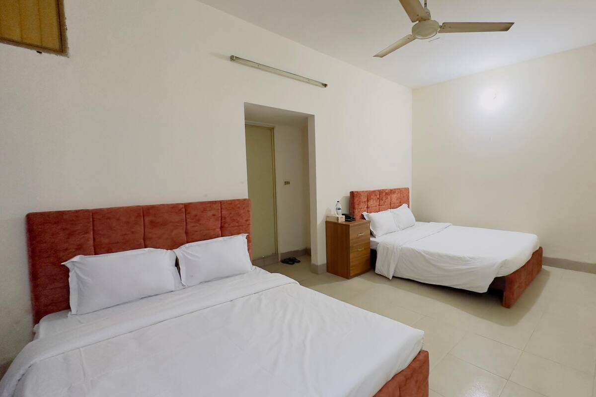 A hotel room with two beds, a ceiling fan, a nightstand, and a door.