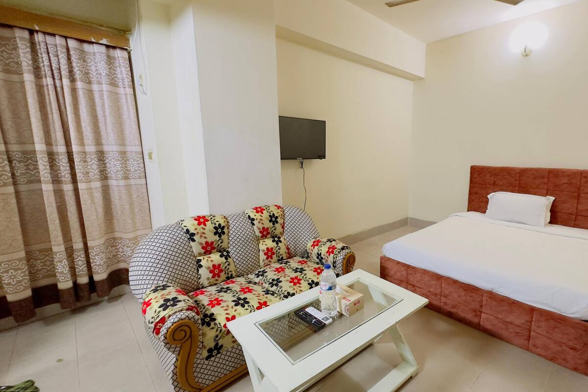 A hotel room with a bed, a sofa, a small table, a TV, and a nightstand.