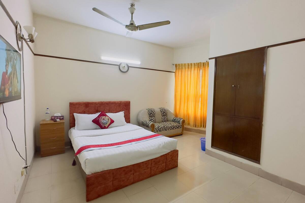 A bedroom with a bed, a wardrobe, a chair, a television, and a ceiling fan.