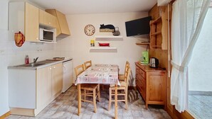 A compact kitchen with a dining table, chairs, a microwave, a clock, and a television.