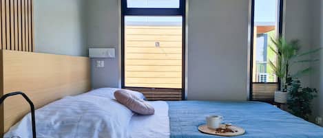 Un dormitorio con una cama, una mesita de noche con un libro, una ventana y una planta.