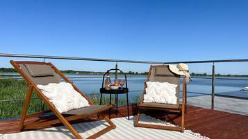 Dos sillones de madera con cojines blancos en una terraza con vista al agua.