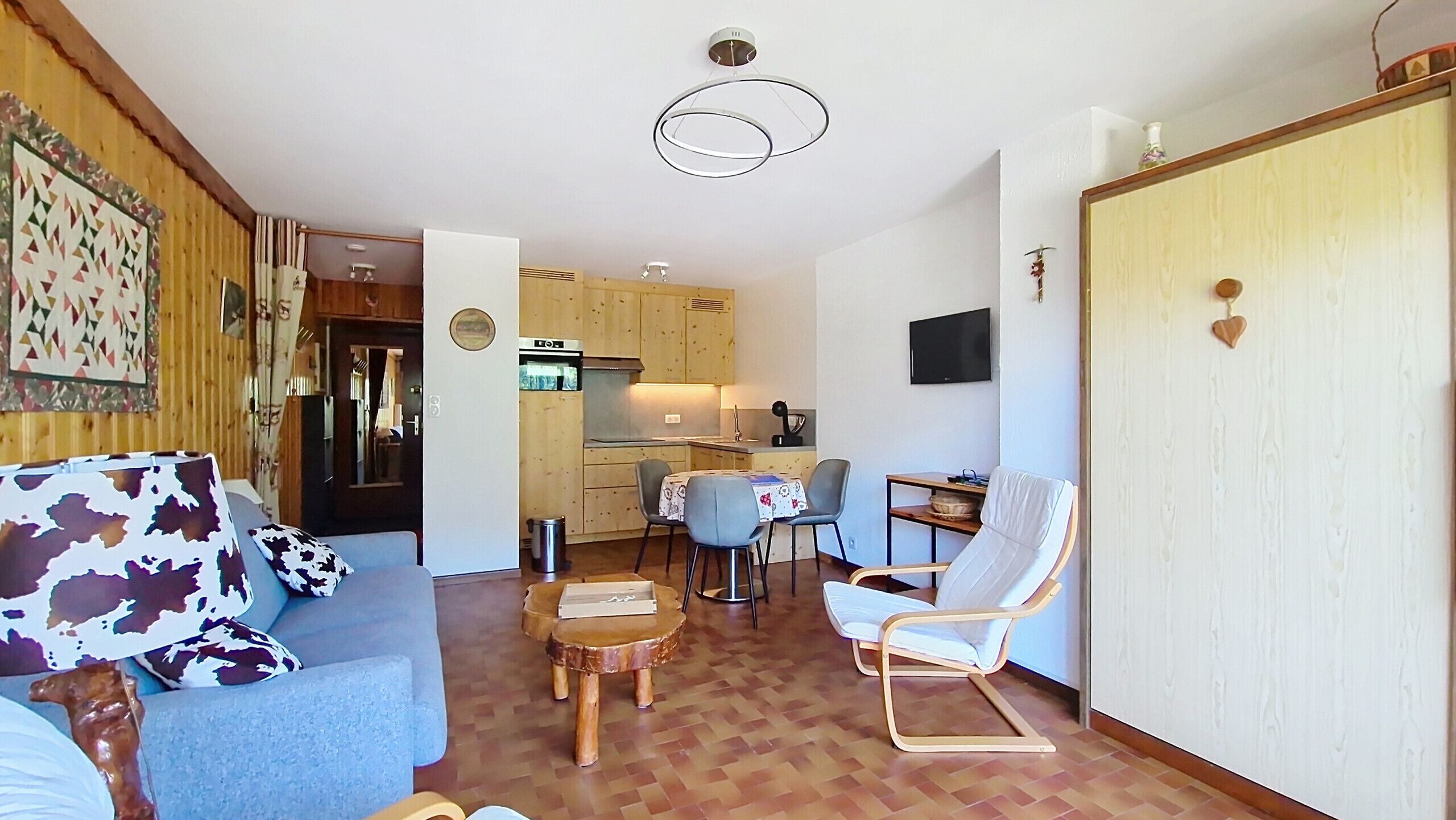 Ein kompakter Wohnraum mit Sofa, Esstisch, Stuhl, Küchenzeile und Wandfernseher.
