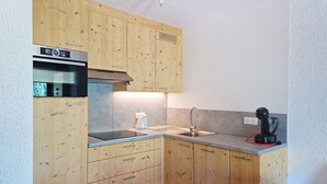 A compact kitchen with wooden cabinets, a built-in oven, a coffee maker, and a sink. - Champs Fleuris CFS7 COSY & VIEW 3 Pers. (Châtel)