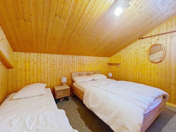 A wooden room with two beds, a nightstand, a lamp, and a mirror.